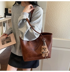 Detalle del bolso tote marrón oscuro de cuero sintético con un tierno colgante de oso