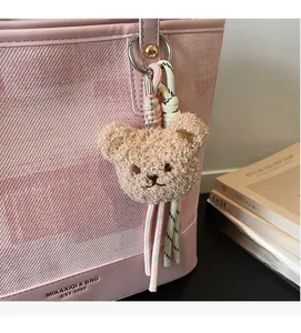Close-up of a fuzzy sherpa bear bag charm with woven rope and metal ring on a pink tote