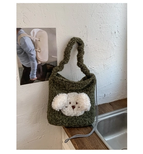 Close-up of plush green bucket bag featuring a white puppy applique and woven drawstring