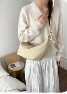 Close-up of beige hobo shoulder bag with knot strap detail worn by model in minimalist studio