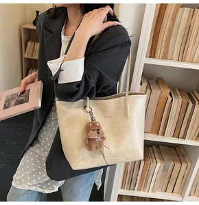 Detalle de bolso tote crema en cuero vintage con un tierno colgante de osito de peluche