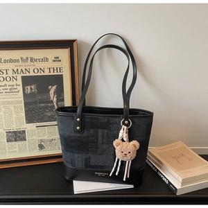 Dettaglio della grande borsa tote con trama denim, finiture in pelle e ciondolo a orsetto