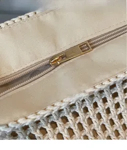 Detailed close-up of smooth gold metal zipper puller on beige woven beach tote bag