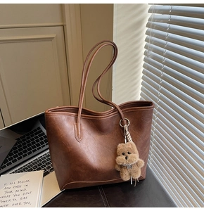 Detalle de bolso tote grande marrón brillante con llavero de peluche de osito