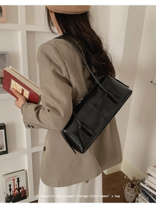 Close-up of black glossy leather baguette bag worn over the shoulder in a vintage style