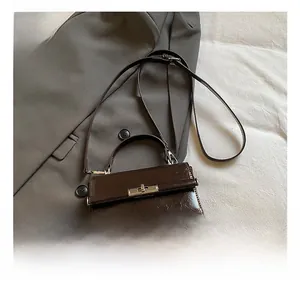 Close-up of a dark brown patent leather handbag with a silver twist-lock on a grey blazer