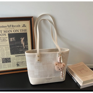 Dettaglio della borsa tote off-white con trama a rete, logo e ciondolo a orsetto