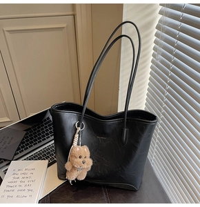 Detalle de bolso tote de cuero negro con logo dorado y colgante de osito de peluche