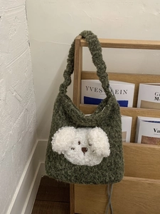 Cute dark green fleece bucket bag with plush puppy design on a wooden wall rack