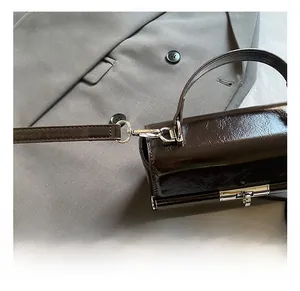 Detailed close-up of dark brown glossy leather texture with silver metal hook and clasp