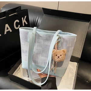 Dettaglio della borsa tote a scacchi blu e bianca con ciondolo a orsetto e logo del marchio