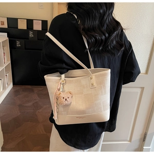 Dettaglio borsa tote in tela crema con finiture in pelle e ciondolo a orsetto