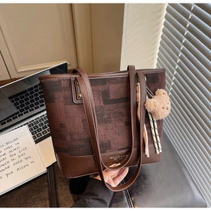 Dettaglio della borsa in tela e pelle con ciondolo orsetto e logo su fondo scuro