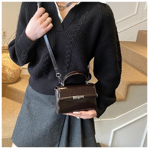 Detail of a dark brown patent leather crossbody bag featuring a silver metal twist lock