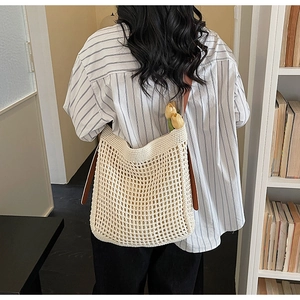Detail of a beige crochet tote bag featuring mesh texture and brown leather strap