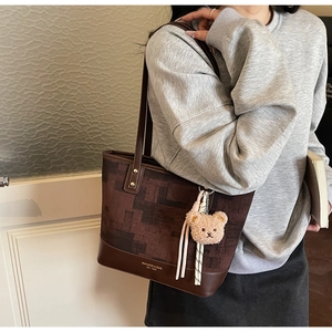 Dettaglio di una borsa tote marrone vintage con ciondolo a orsetto su una modella