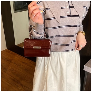 Detailed view of burgundy patent leather square handbag with silver twist lock and handle