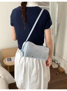 Detail of light blue cylinder crossbody bag with star rivets and heart charm on a model