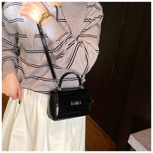 Close-up of black patent leather crossbody bag with silver twist lock on model