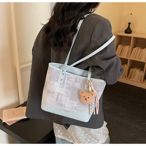 Dettaglio della borsa tote in pelle blu e tessuto con ciondolo a orsetto e nappa
