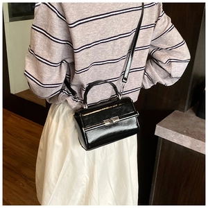 Detailed view of black glossy mini square bag with silver metal lock on a model outfit