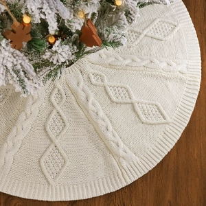 Jupe de sapin de Noël en tricot torsadé ivoire sur un sol en bois sombre avec lumières