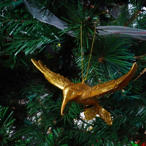 Golden hummingbird Christmas ornament with glitter finish hanging on a green tree branch