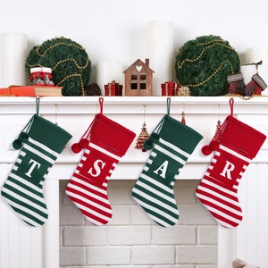 Set of 4 knitted Christmas stockings with T/S/A/R initials and pompoms on a fireplace
