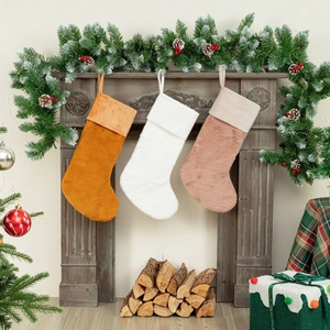 Three soft plush Christmas stockings in orange, white, and pink hanging on a wooden fireplace