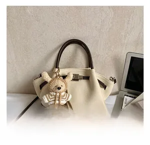 Detailed view of cream pebble leather tote with brown handles and a cute bear charm