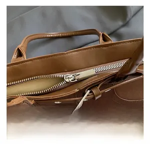 Close-up of brown leather bucket bag showing silver metal zipper and buckle details