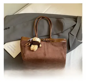 Detail of dark brown suede tote bag featuring a leather buckle and a cute bear charm
