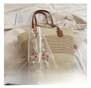Detail of beige straw tote bag with brown leather handles and floral lace scarf decoration