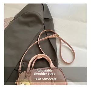 Detail view of pink Boston bag with textured leather and a cute brown bear charm accessory