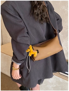 Détail d'un sac bandoulière en cuir marron avec breloque cheval jaune et logo doré