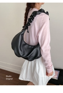 Detailed view of black pleated dumpling bag with ruffled shoulder strap on model