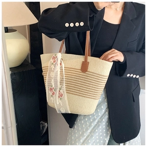 Detail of striped straw tote bag featuring leather handles and white lace floral ribbon