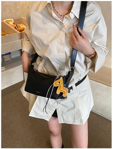 Détail d'un sac porté épaule noir avec un charm de cheval jaune et le logo de la marque