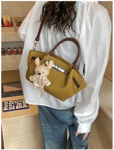 Detail of olive green leather handbag with silver lock and teddy bear charm on model