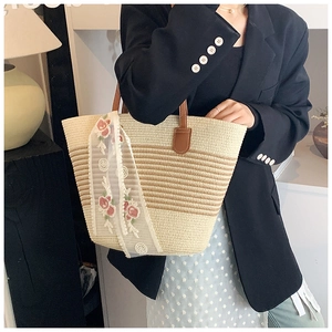 Close-up of woven straw tote bag with floral lace ribbon and brown leather handles