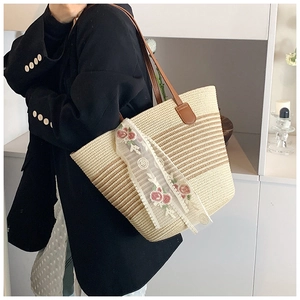 Detail of beige straw tote bag featuring pink floral lace ribbon and brown leather handle