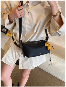 Détail du sac bandoulière en cuir noir avec zip doré et breloque petit cheval jaune