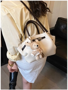 Detail of white lychee leather handbag with silver buckle and brown handle and bear charm