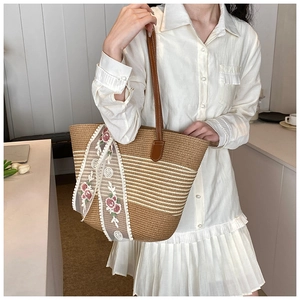 Detail of floral lace embroidery and woven straw texture on a brown beach tote bag
