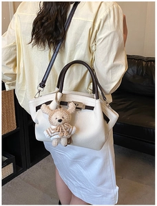 Close-up of cream leather tote with brown handles, metal lock, and bear charm accessory