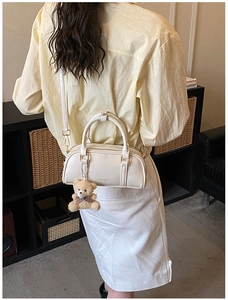 Détail du sac à main plissé blanc crème avec boucle dorée et breloque en peluche