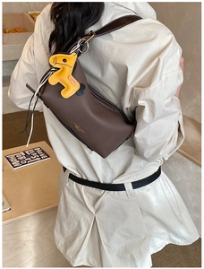 Détail d'un sac bandoulière marron mat avec breloque cheval jaune et large bandoulière