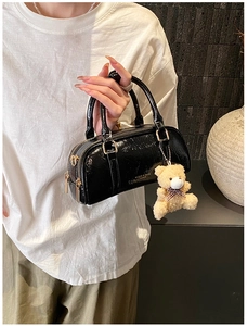 Detail of glossy black patent leather boston bag featuring a cute teddy bear charm