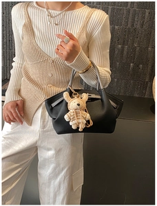 Detail of black leather handbag with a light brown knitted bear charm and silver hardware