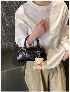 Close-up of black glossy Boston bag with crinkle texture and cute teddy bear charm